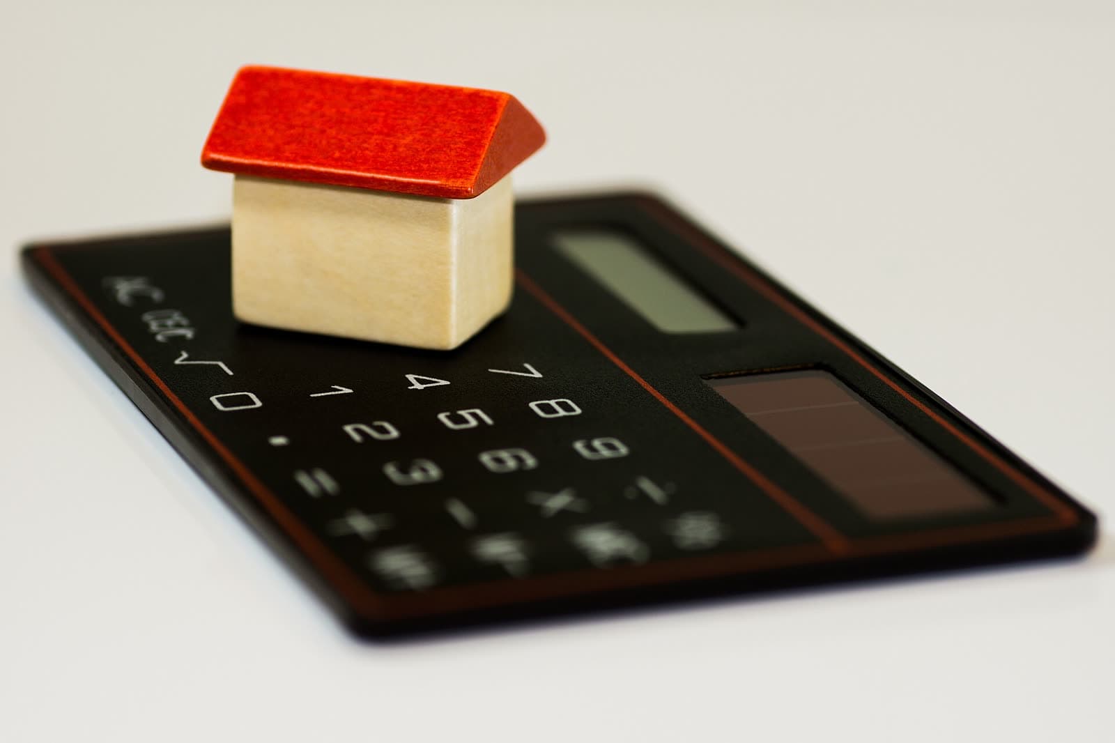 A small wooden house resting on a black calculator